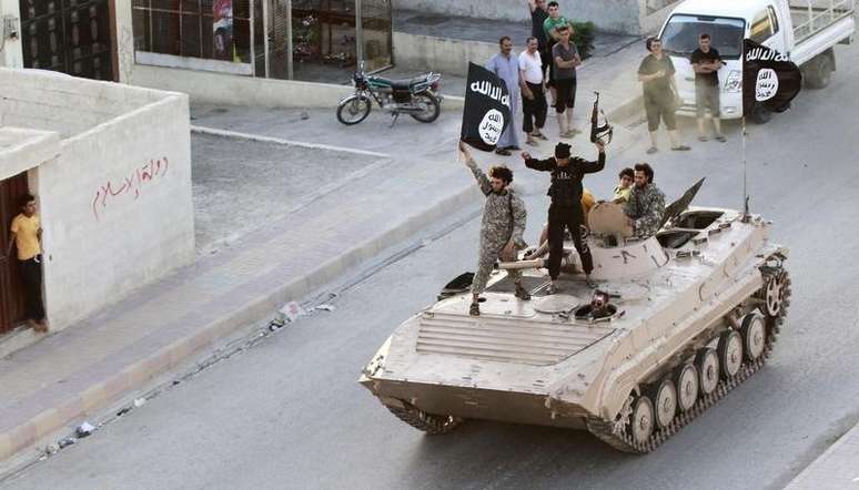 <p>Militantes do Estado islâmico com uma bandeira do EI durante um desfile militar na província de Raqqa</p>