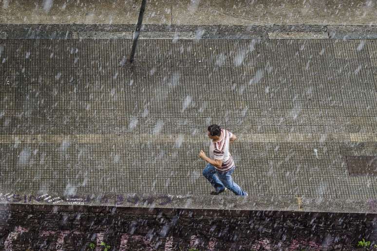 Homem corre da chuva na região central de São Paulo