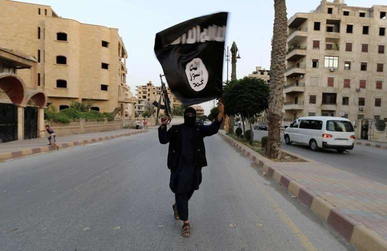 <p>Integrante do Estado Islâmico carrega bandeira do grupo em Raqqa, na Síria</p>