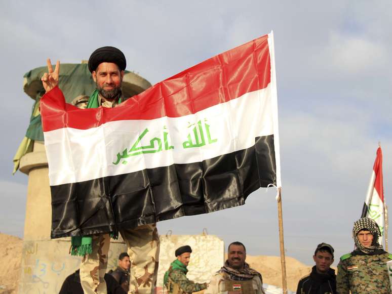 <p>Soldado iraquiano ergue símbolo de vitória próximo à bandeira nacional em Tikrit, Iraque</p>