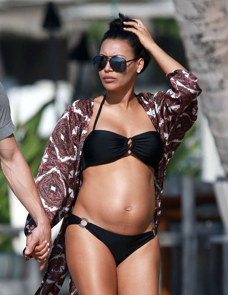 Famosa por viver Santana no seriado Glee, Naya Rivera foi fotografada em uma praia do Havaí com seu marido Ryan Dorsey. A atriz, que está grávida, usou um biquíni preto que mostrou sua barriga.