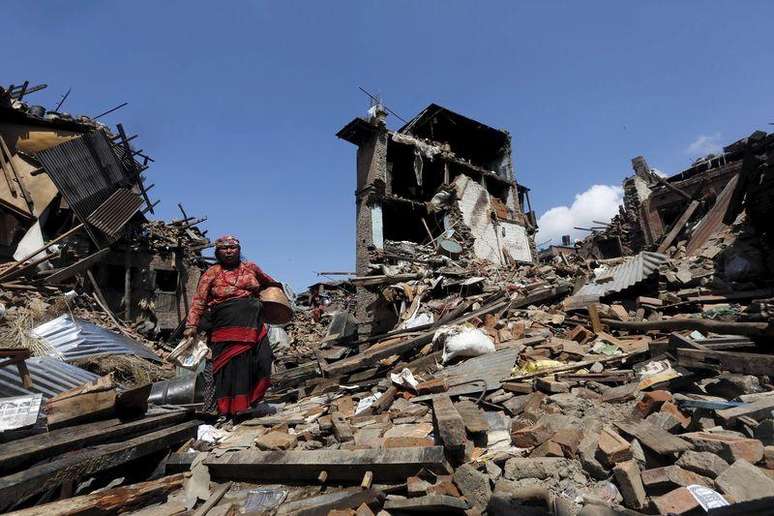 Mulher carregando seus pertences em meio a destroços por conta do terremoroto no Nepal