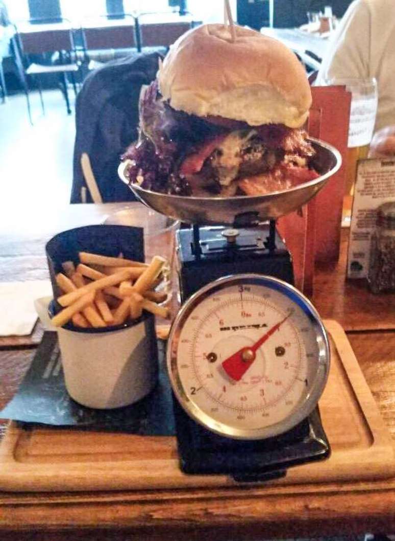 O restaurante serve o hambúrguer na balança e as batatas em uma caneca
