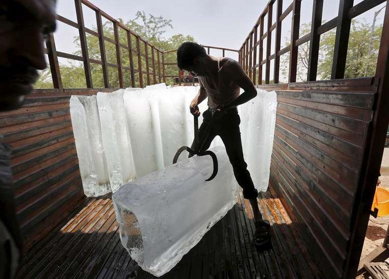 Trabalhador corta gelo para resfriamento de alimentos em mercado na Índia.   19/05/2015