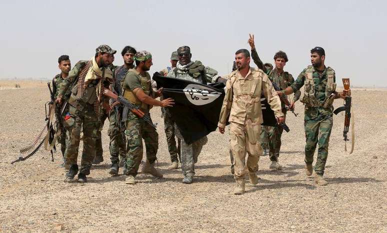 Paramilitares xiitas iraquianos e soldados iraquianos seguram bandeira do Estado Islâmico