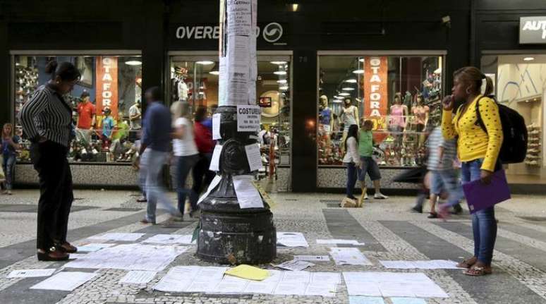 Pessoas olhando ofertas de emprego coladas em um poste no centro de São Paulo