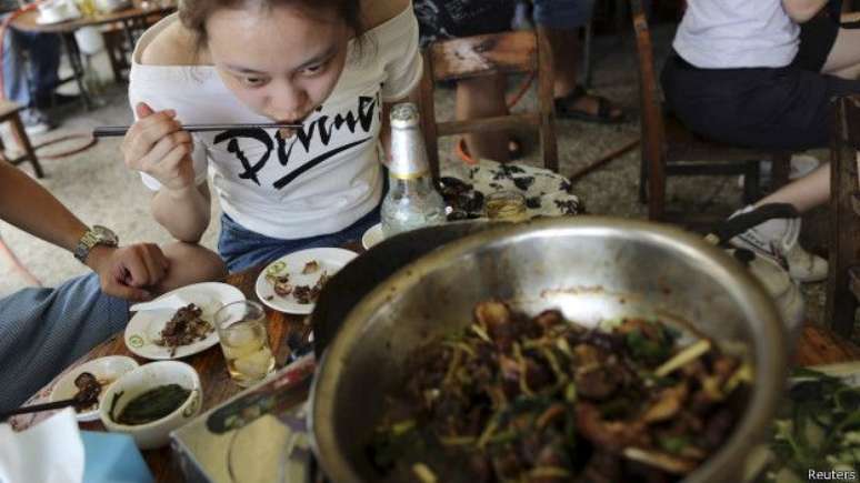 Mulher come carne de cachorro; defensores do festival dizem que prato é tradicional na China