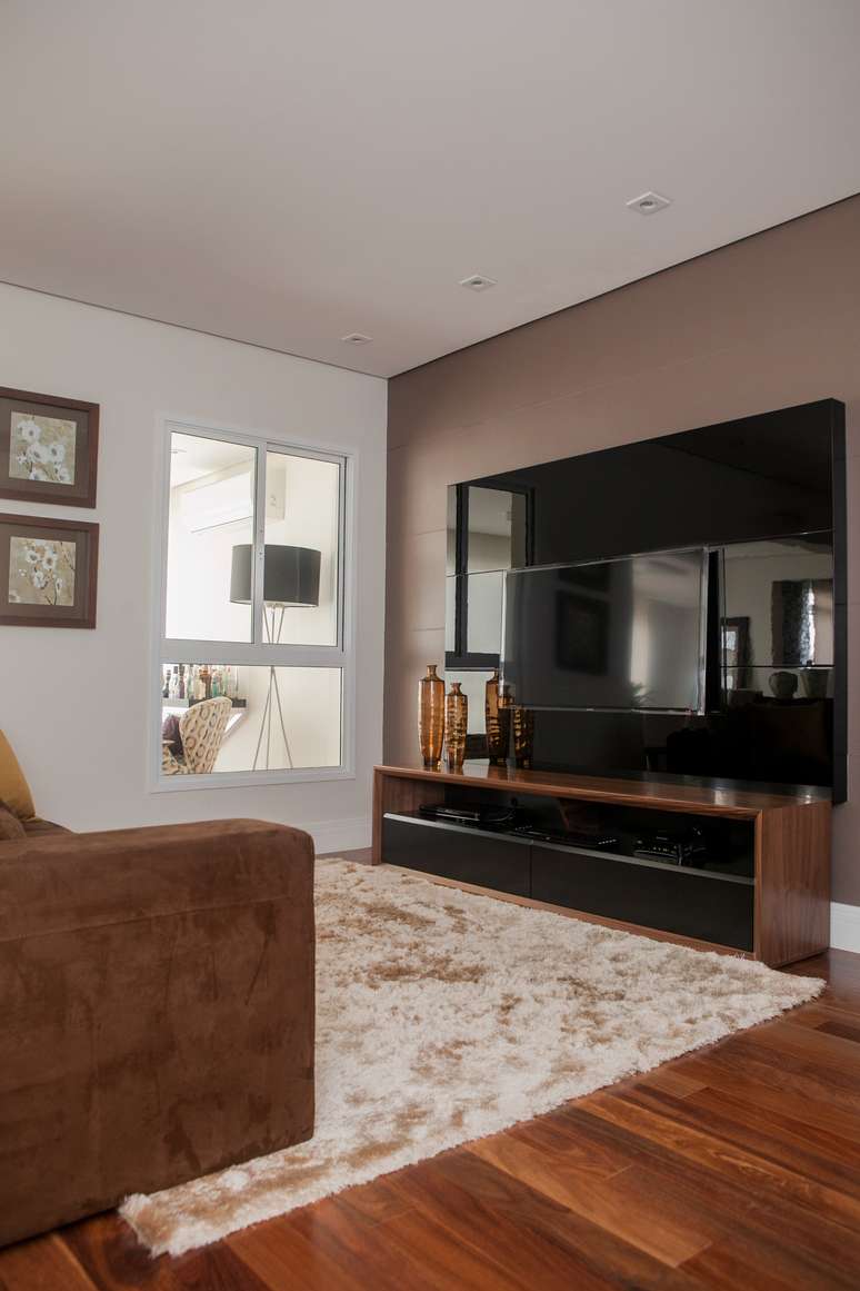 Rack com pouca profundida e TV na parede ajudam a aproveitar o espaço restrito; teto branco, cores neutras e rodapé da cor da parede ajudam a dar amplitude ao ambiente