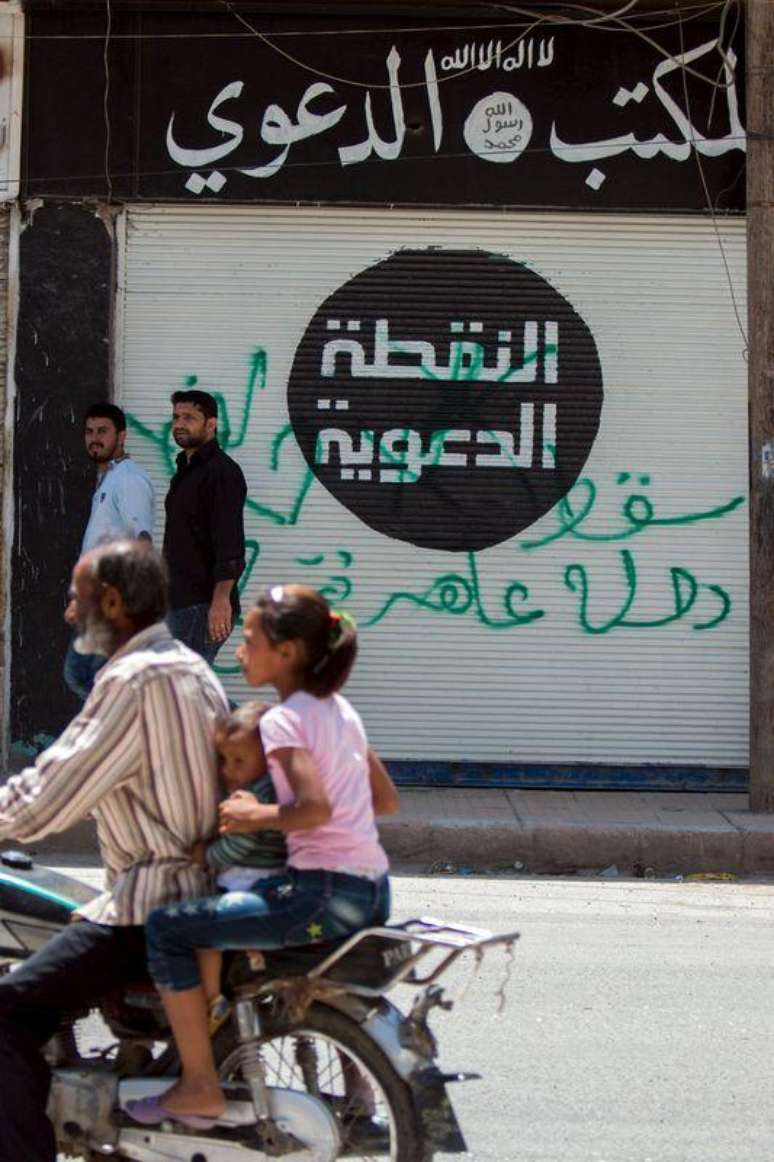 Civis em uma moto passam em frente a um escritório que pertenceu a combatentes do Estado Islâmico, em Tel Abyad. 19/06/2015