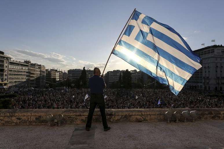 Homem agita a bandeira da Grécia durante manifestação na frente do Parlamento, em Atenas