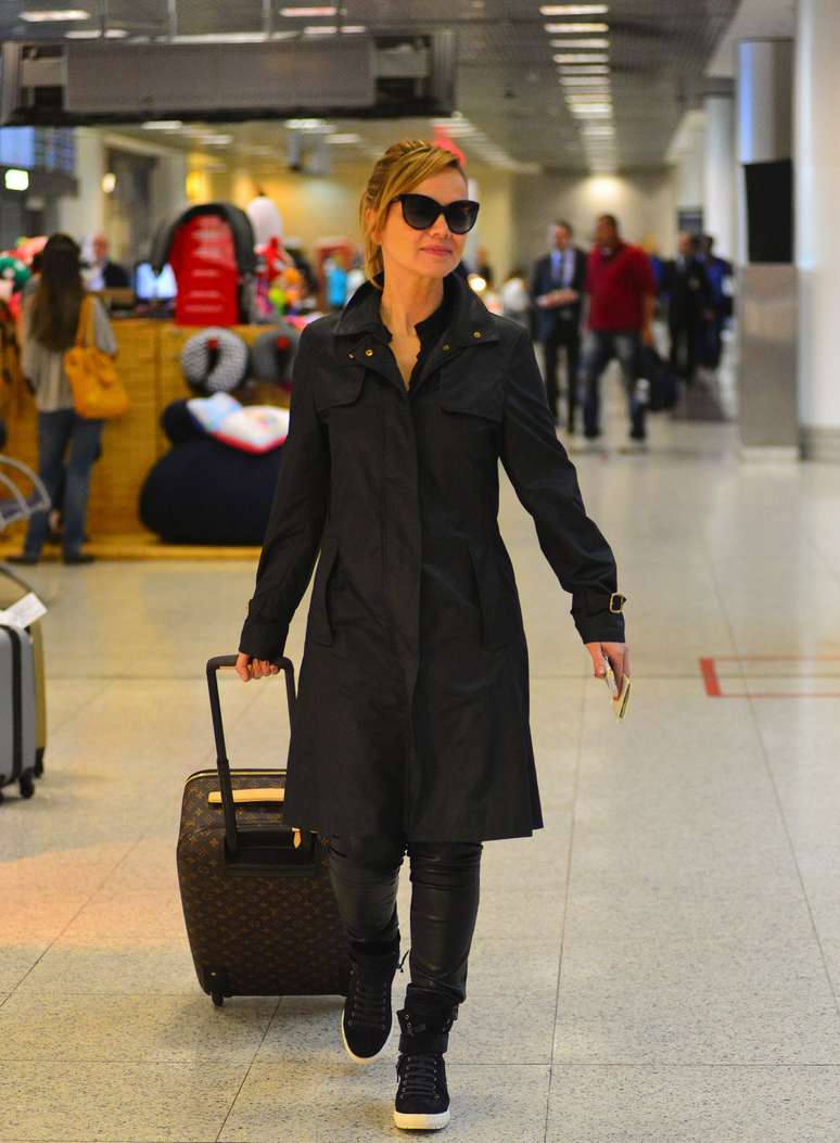 Eliana fez uma boa escolha para pegar o avião, com o trench-coat preto fechado, calça justa com textura que lembra couro e tênis. Conforto e elegância juntos.