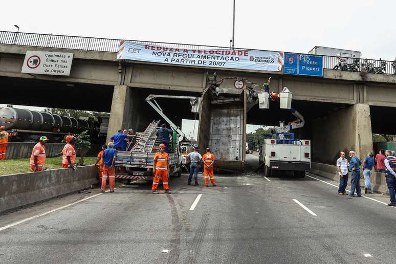 Homens da Defesa Civil tentam cortar caçamba de caminhão que bateu na Ponte do Piqueri