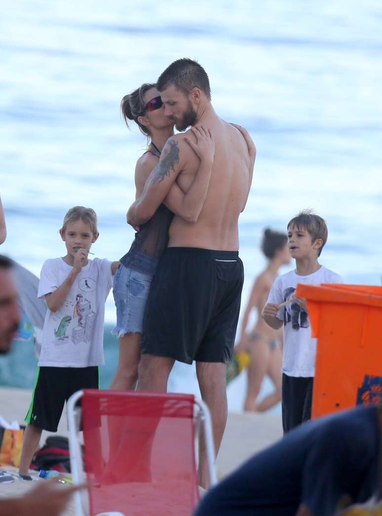 Fernanda Lima beija Rodrigo Hilbert no rosto, enquanto os filhos assistem a cena na praia do Leblon, no Rio de Janeiro, neste domingo (19)