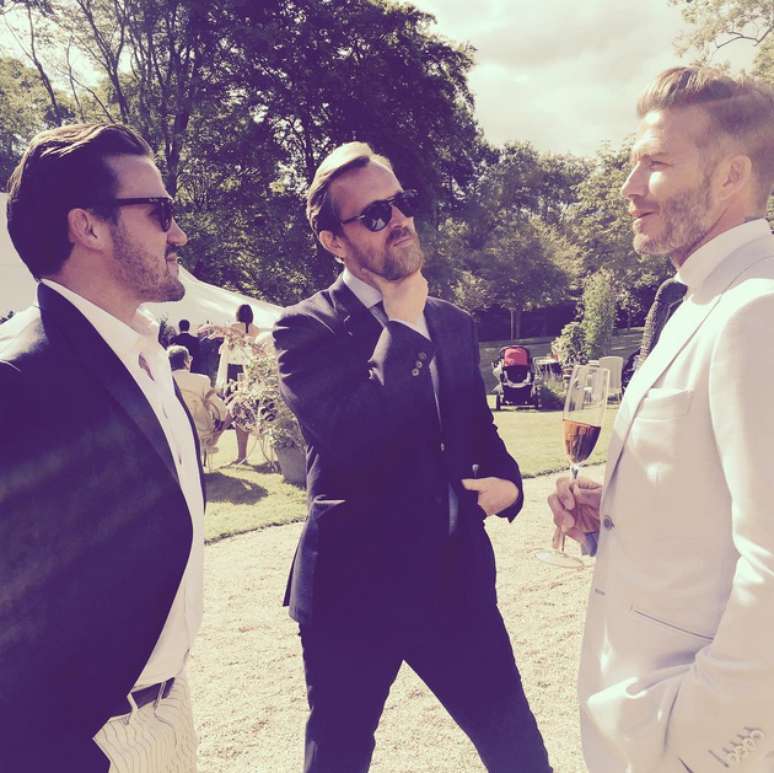 Segurando taça de champanhe, David Beckham conversa com amigos durante a festa 