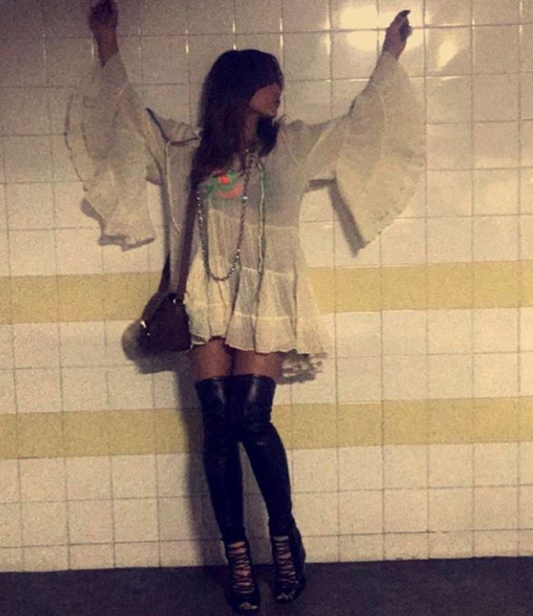 O vestido tipo bata com mangas amplas é outra referência ao estilo &#039;boho chic&#039;, ainda mais com as botas acima dos joelhos, mas o look fica muito datado e propício para uma festa temática