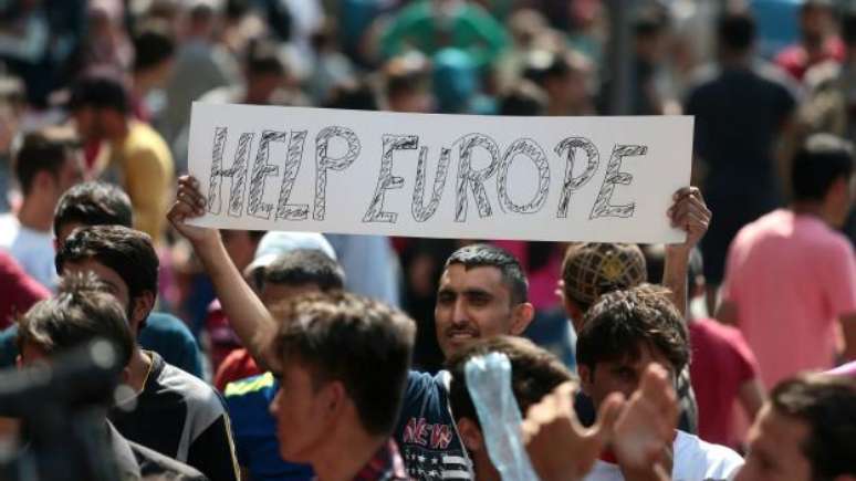Homem exibe cartaz com a frase 'Ajude, Europa' enquanto centenas de refugiados e imigrantes esperavam permissão para embarcar em trens em Budapeste