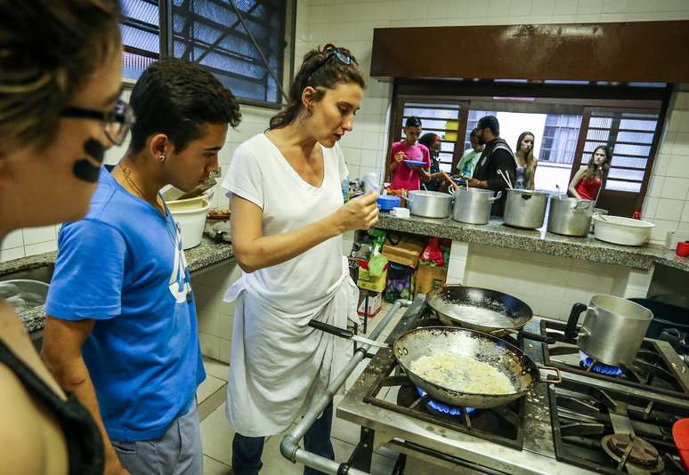 Paola conversa com estudante enquanto cozinha