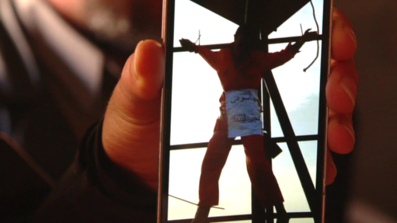 Líbio mostra no celular imagem de seu irmão, que teria sido morto a tiros e crucificado pelo EI