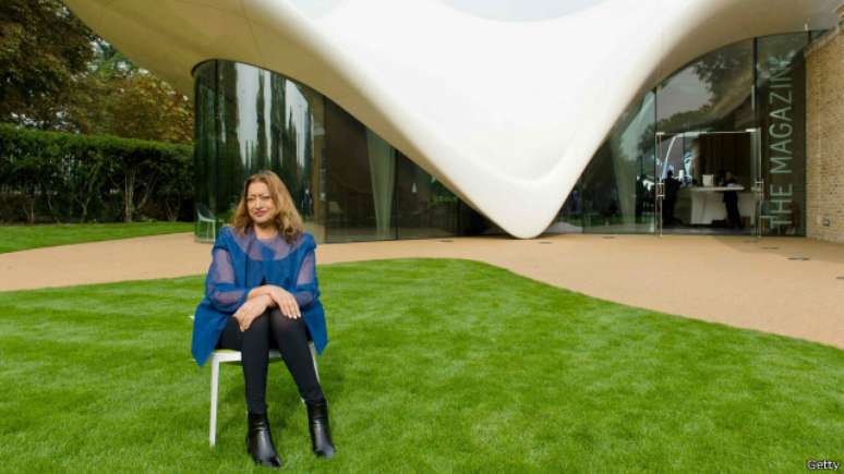 Zaha Hadid em frente a um de seus projetos com as curvas características de seu estilo