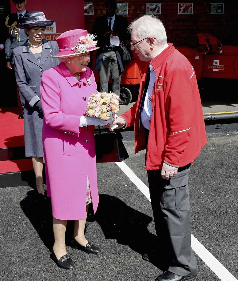 Rainha Elizabeth II atende ao mais antigo carteiro da Grã-Bretanha, Bob Hartley, em visita aos correios durante as comemorações de seu 90° aniversário.