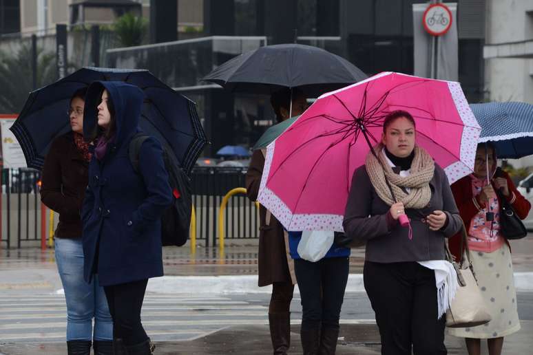 Pedestre se protege do frio e da garoa na avenida Paulista, em São Paulo (SP), na manhã desta terça-feira (24)