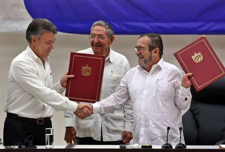 O delegado das Farc em Cuba, Rodrigo Londoño Echeverri (dir.), e o presidente da Colômbia, Juan Manuel Santos (esq.), junto ao presidente de Cuba, Raúl Castro, seguram o acordo de paz entre o governo e a guerrilha durante cerimônia em Havana