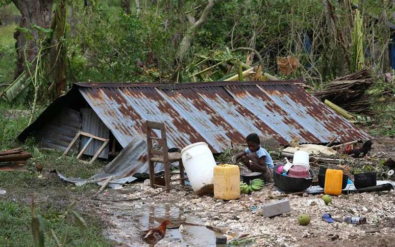 Criança cozinha ao lado de casa destruída pelo furacão Matthew no Haiti