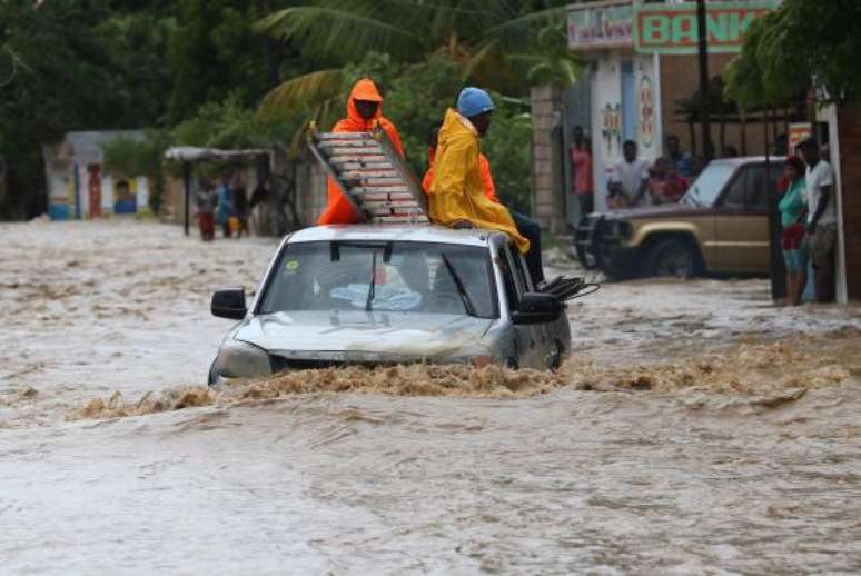 Um grupo de pessoas tenta cruzar uma via alagada in Leogane, no Haiti, após a passagem do Furacão Matthew -