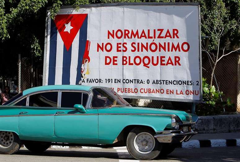 Havana: carro antigo passa em frente a cartaz alusivo ao bloqueio econômico imposto pelos Estados Unidos a Cuba