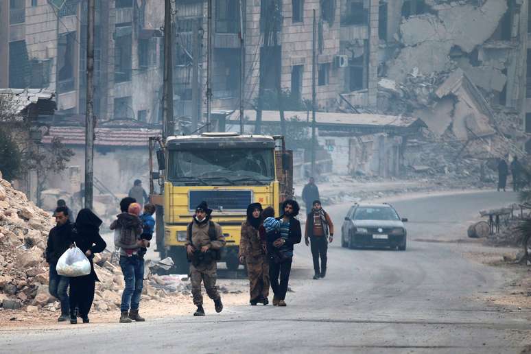 Combatente rebelde passa por pessoas que levam pertences enquanto fogem mais para dentro das áreas remanescentes de Aleppo.