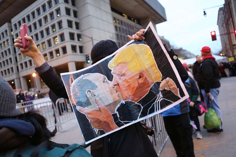 Homem protesta contra Donald Trump segurando cartaz do presidente eleito beijando Putin