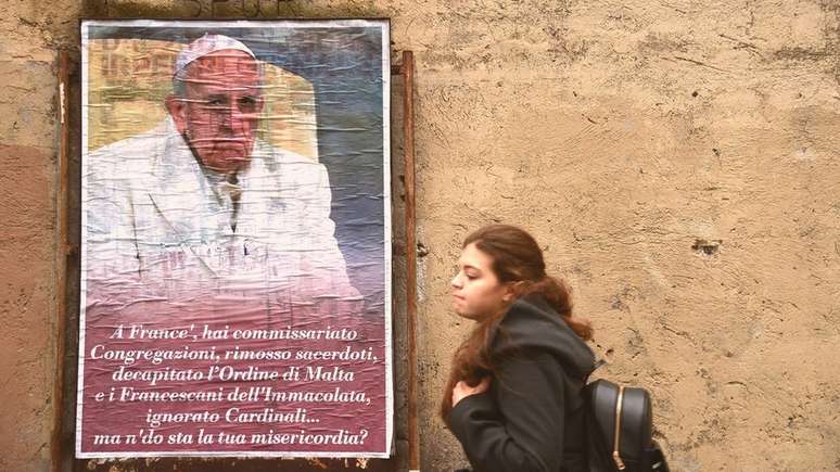 Mulher passa por cartaz com críticas ao papa Francisco
