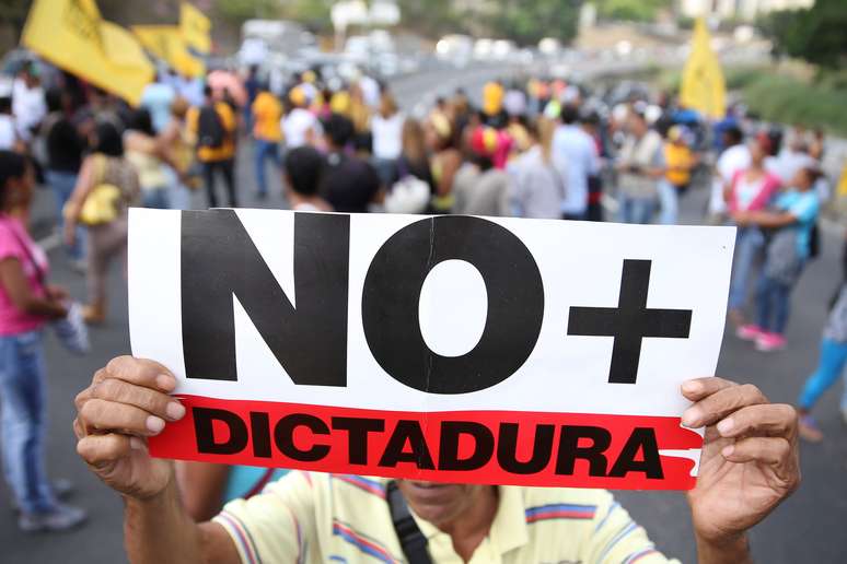 Opositor de Nicolás Maduro segura placa contra a ditadura durante protesto na Venezuela