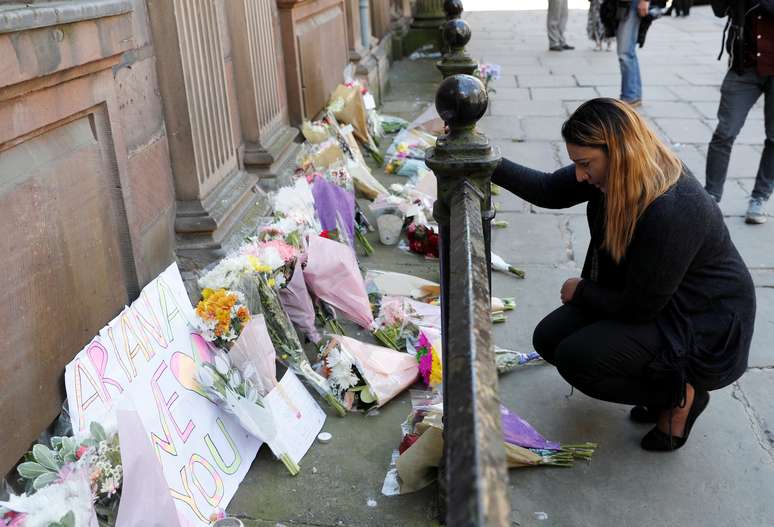 Mulher deposita flores em homenagem às vítimas do atentado após show de Ariana Grande em Manchester.