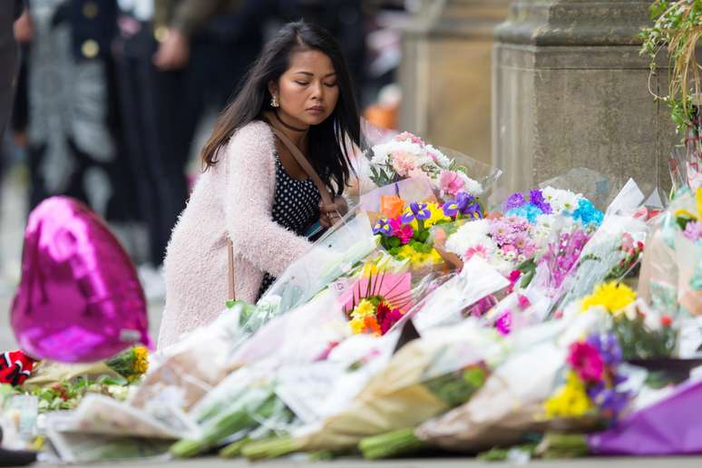 Mulher deposita flores em homenagem às vítimas do atentado após show de Ariana Grande em Manchester.