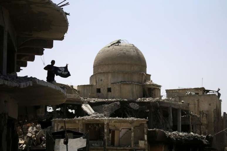 Membro das forças de segurança iraquianas segura a bandeira de militantes do Estado islâmico no topo de um edifício destruído em confrontos na Cidade Velha de Mosul, no Iraque10/07/ 2017. REUTERS/Thaier Al-Sudani     