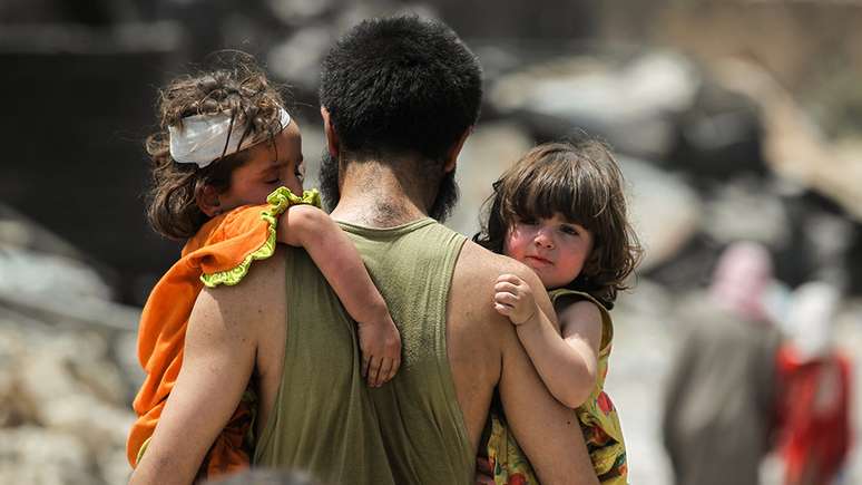 Homem carrega crianças em Mossul