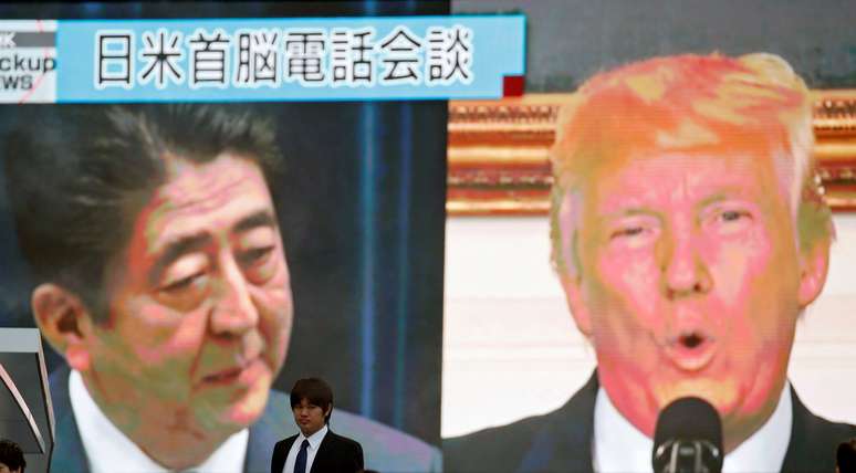 Homem passa diante de telão com as imagens do premiê japonês, Shinzo Abe, e do presidente dos EUA, Donald Trump, em Tóquio