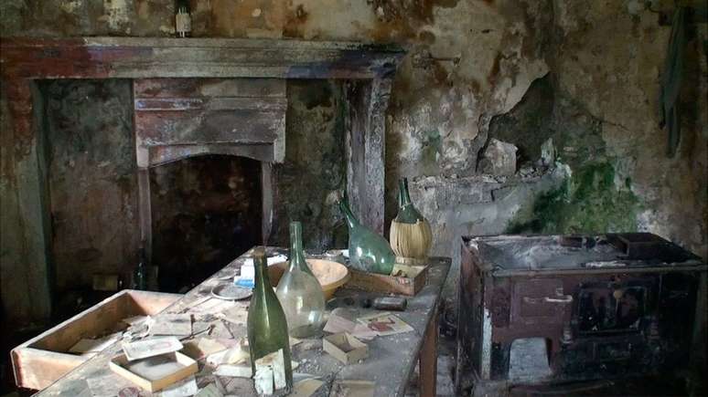 Interior de casa abandonada em Corippo, com ladeira e garrafas vazias em uma mesa