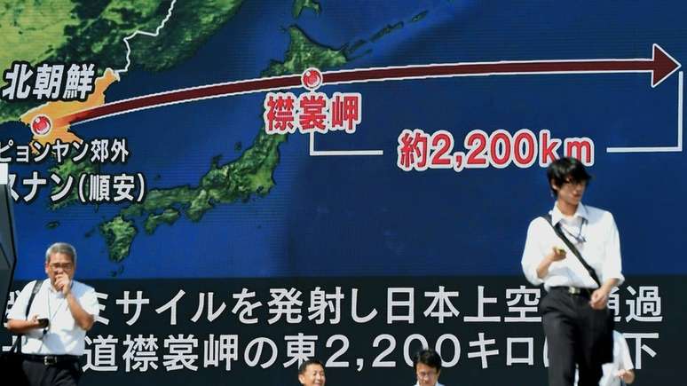 Cidadãos japoneses em frente a uma grande tela que mostra a trajetória do ultimo míssil norte-coreano