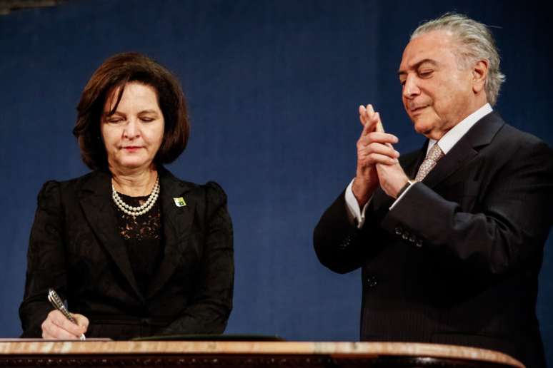 Raquel Dodge assina documento em um púlpito ao lado de Michel Temer