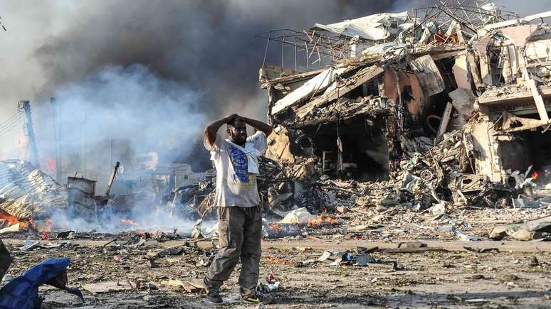 Homem põe as mãos na cabeça ao lado de ruínas e corpos na Somália