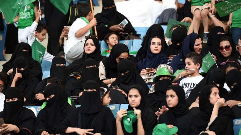 Mulheres sentadas na arquibancada de um estádio com seus filhos