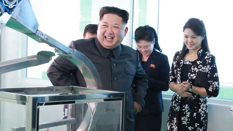 Kim Jong Un rindo e a mulher atrás dele ao lado de outras duas pessoas