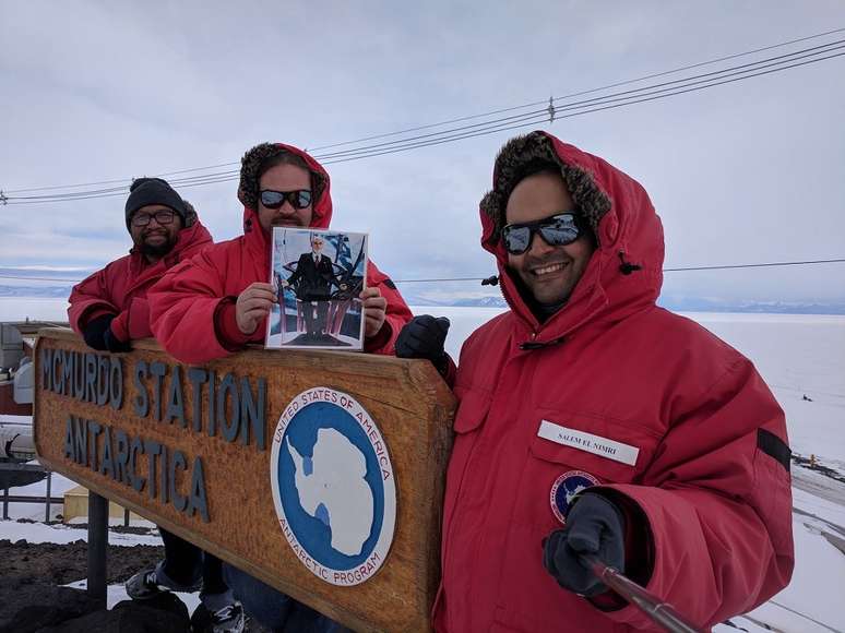 Equipe da NASA posa para selfie em grupo na placa de entrada da Estação McMurdo, na Antártica