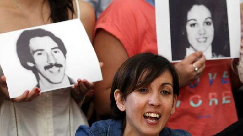 Ativistas seguram fotos dos pais de Adriana, que desapareceram em 1977