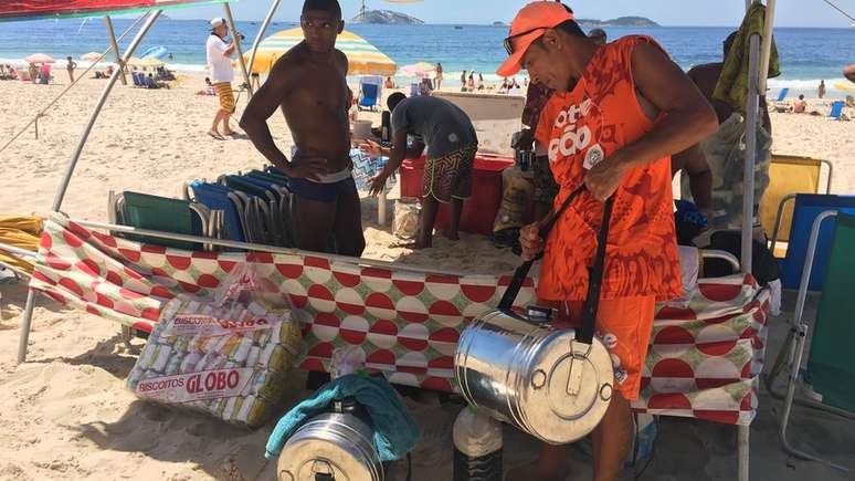 Na praia, Souza armazena uma parte do mate em uma barraca e sai para a venda com 5 litros no galão cheio de gelo; quando acaba, ele volta até a barraca para reabastecer | Foto: Ana Terra Athayde/BBC