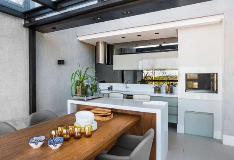 30. Casa com varanda gourmet com mesa de madeira e poltronas. Projeto de Leonardo Muller