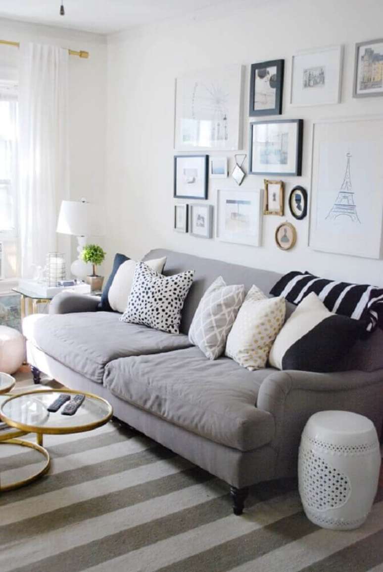 32. Decoração de sala em tons de cinza e branco com muitos quadros e almofadas.