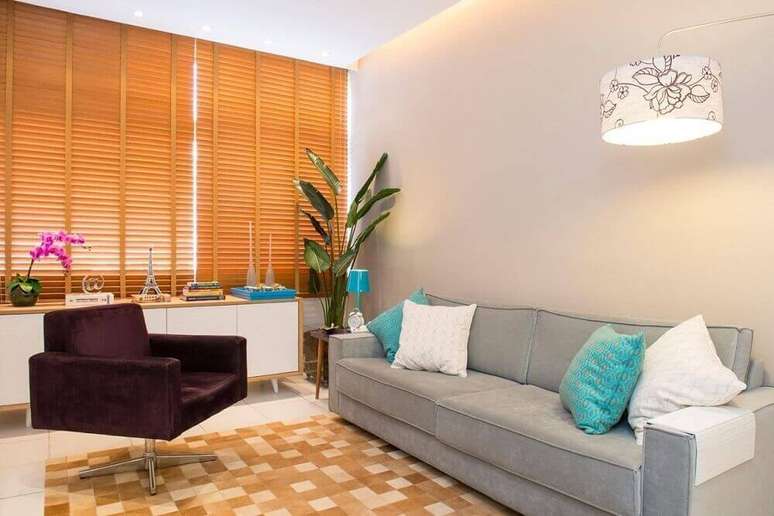 4. Sala de estar decorada com persiana de madeira, sofá cinza e poltrona bordô.